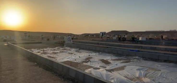 Sunset over kerbed bays lined with white polythene sheet, distant workers in hi-vis along far kerb line