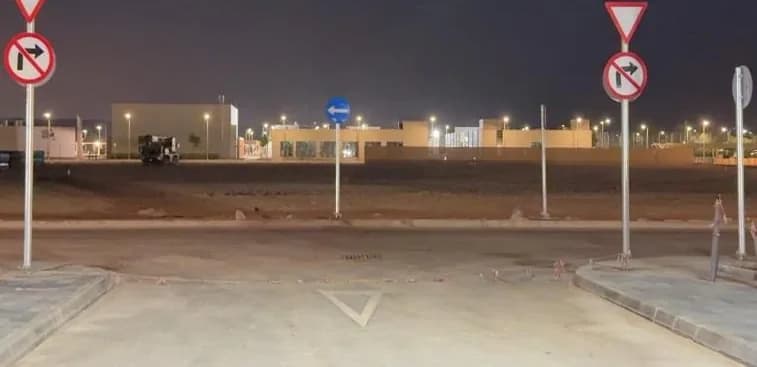 Newly installed give-way, no-right-turn and keep-left signs at a parking exit onto a road at night, truck parked in distance