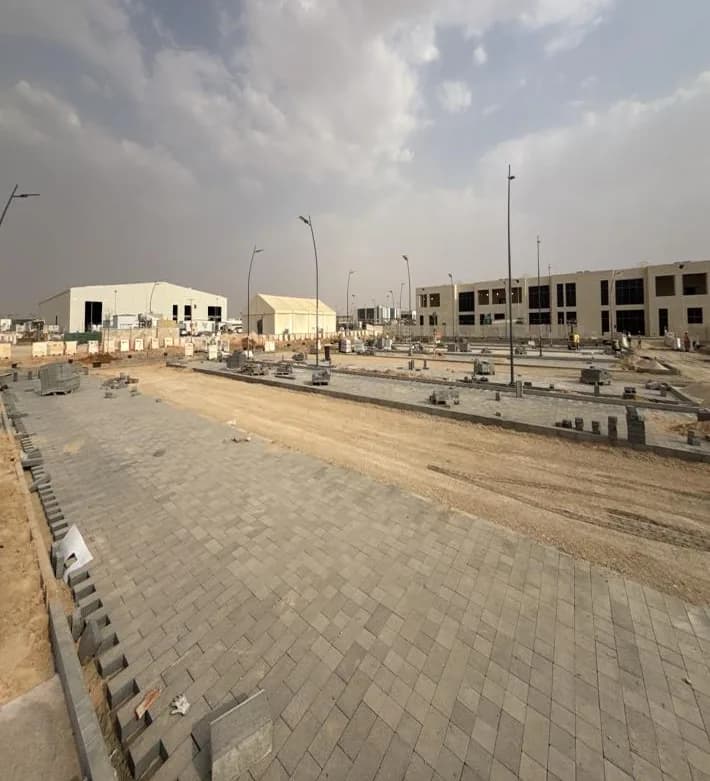 Interlock pavement completed along the parking frontage. Wide interlock pavement with kerb edging, haul road and kerbed bays beyond, warehouse, tent and two-storey building on the skyline