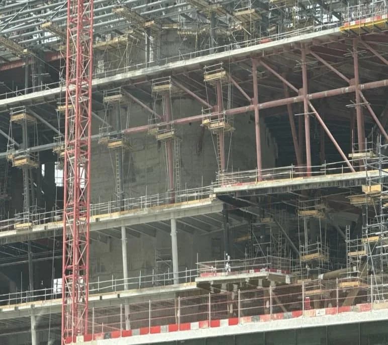 Close view of red tower crane mast beside steel roof trusses, scaffolding and concrete floors of multi-storey structure