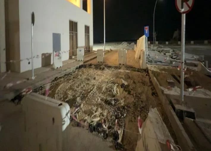 Night view of the Qiddiya building with its logo and a no-parking sign; graded strip with dark sheeting and warning tape in the foreground