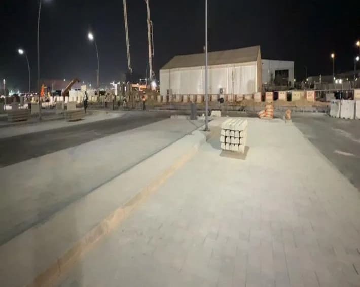 Finished interlock walkway and roadway at night with the pump boom over the tent in the background and stacked kerb units; distant tiny figures