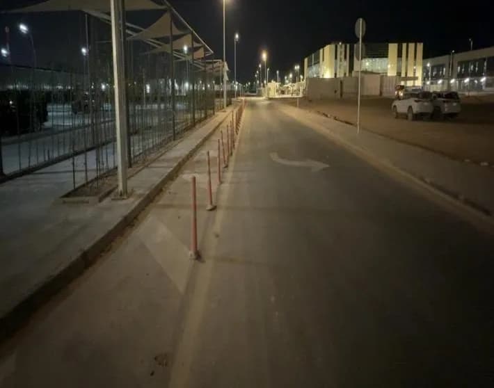 Night road with delineators, shade canopies over parking, lit buildings, parked pickups at right